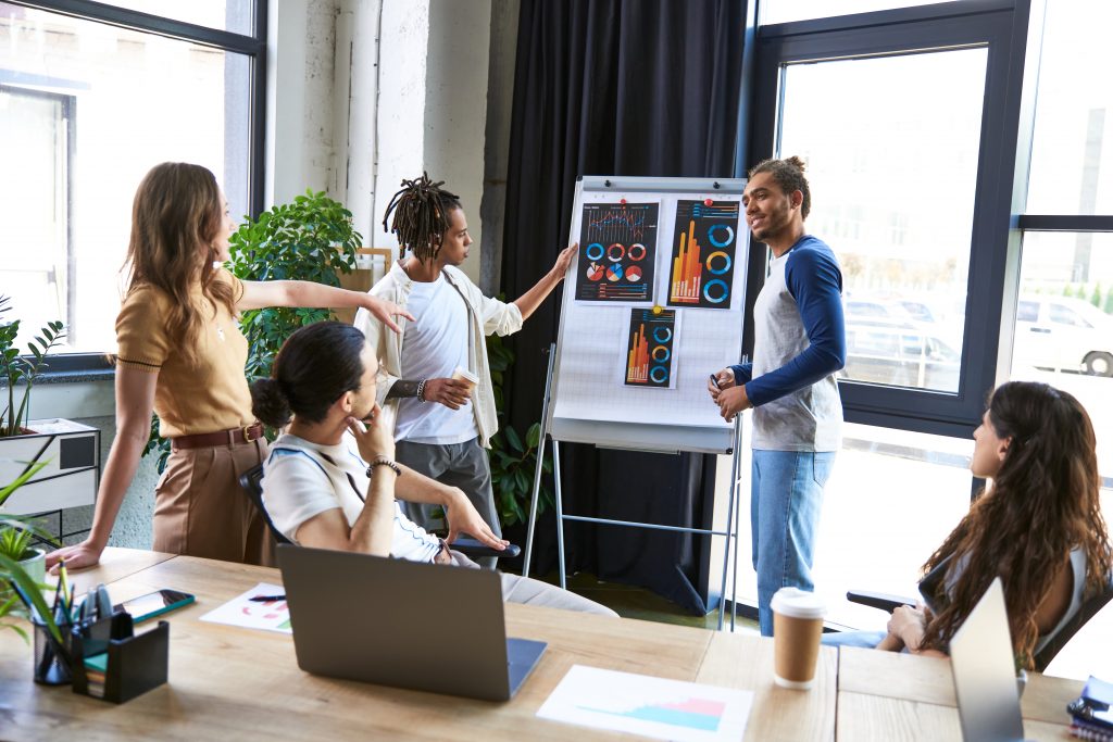 businesswoman pointing at flip chart with graphs near multiethnic team working on project in office