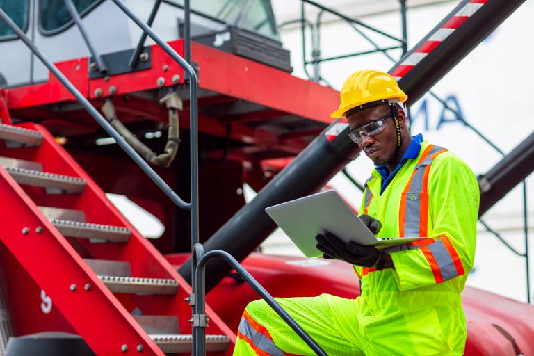 african black worker in cargo port shipping industrial in yellow hard hat safety vest on duty. foreman or supervisor in container ship yard terminal.