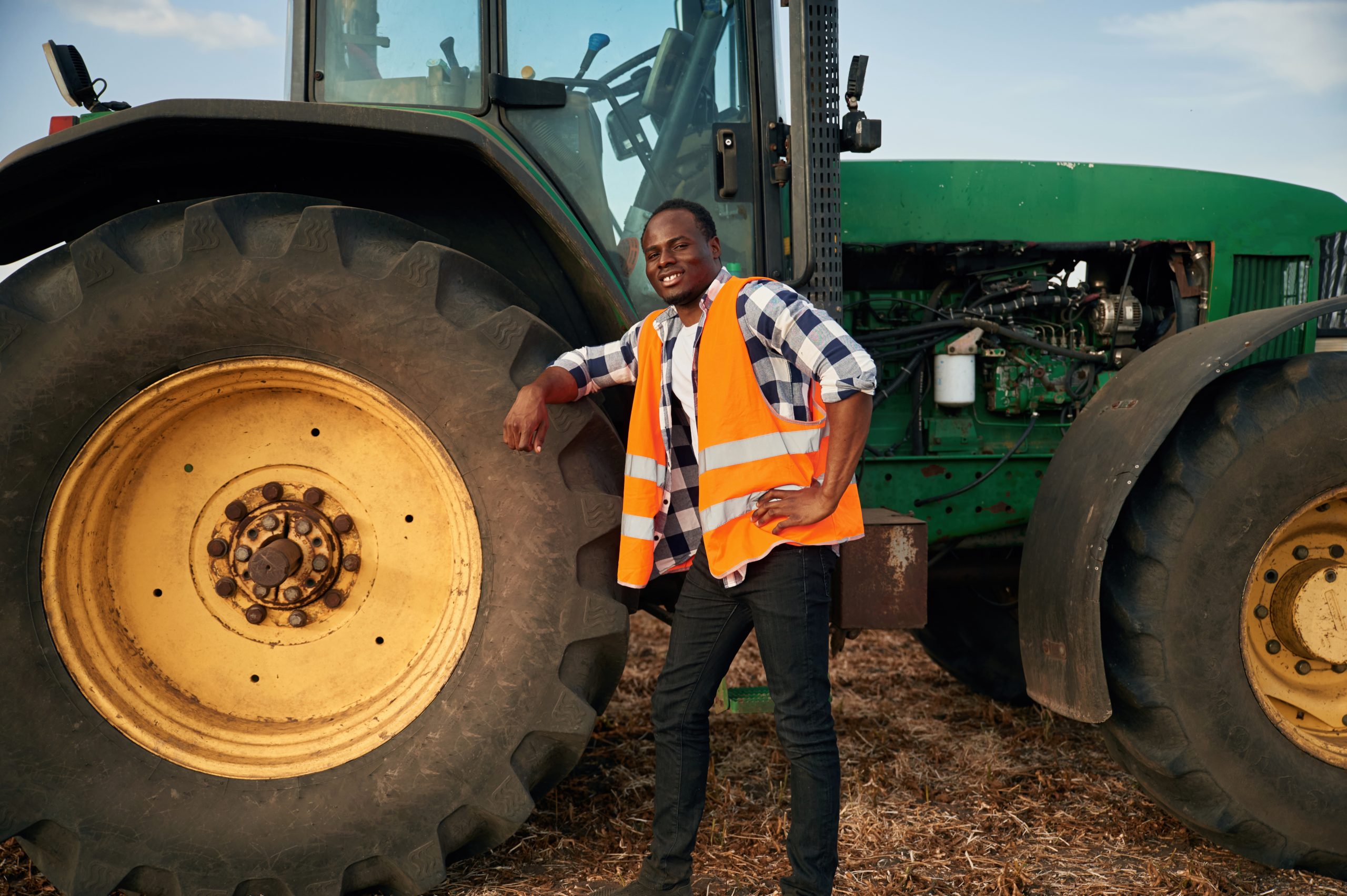 leaning on the big wheel of tractor. beautiful african american man is in the agricultural field