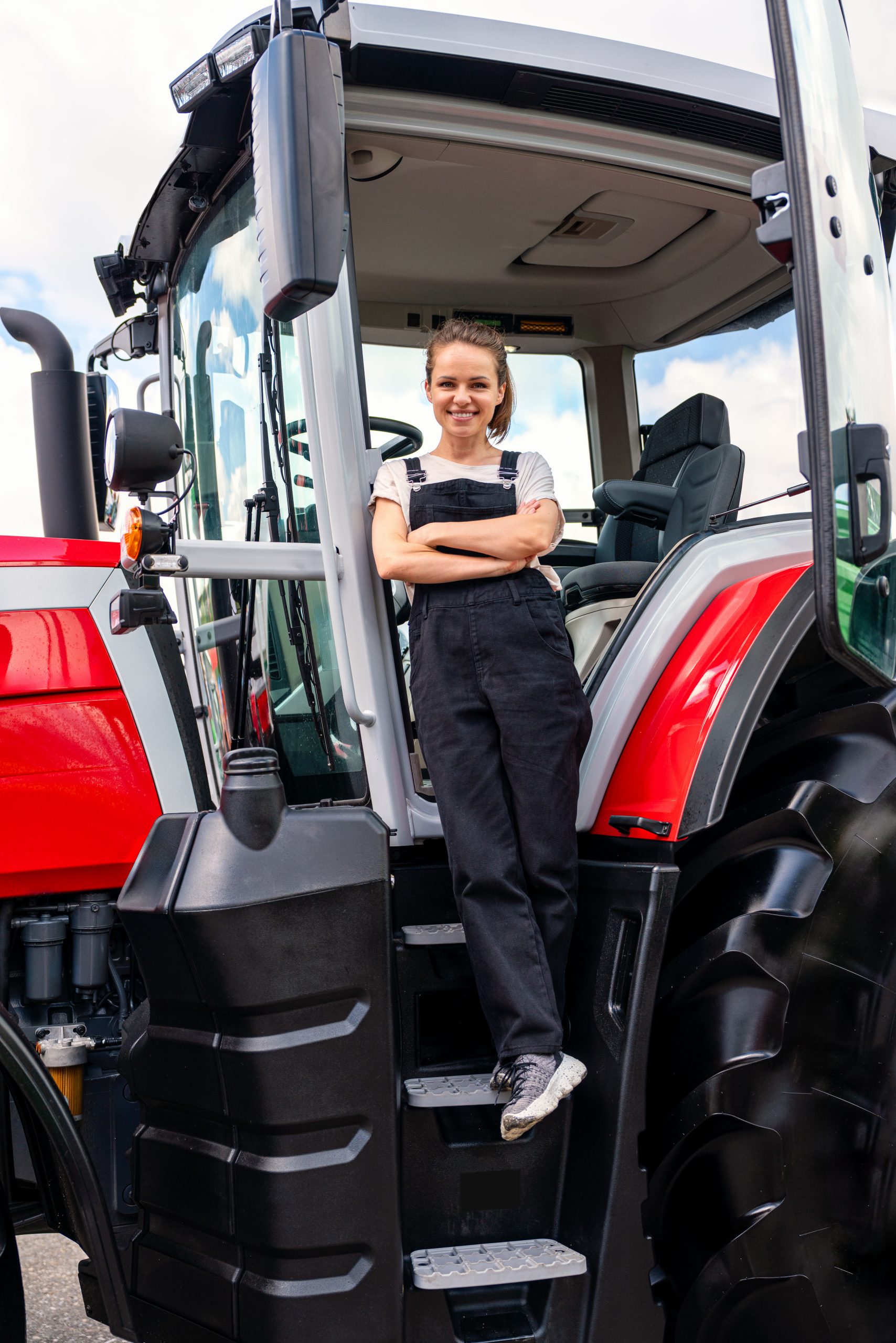 vertical portrait of female farm worker next to tractor outdoors